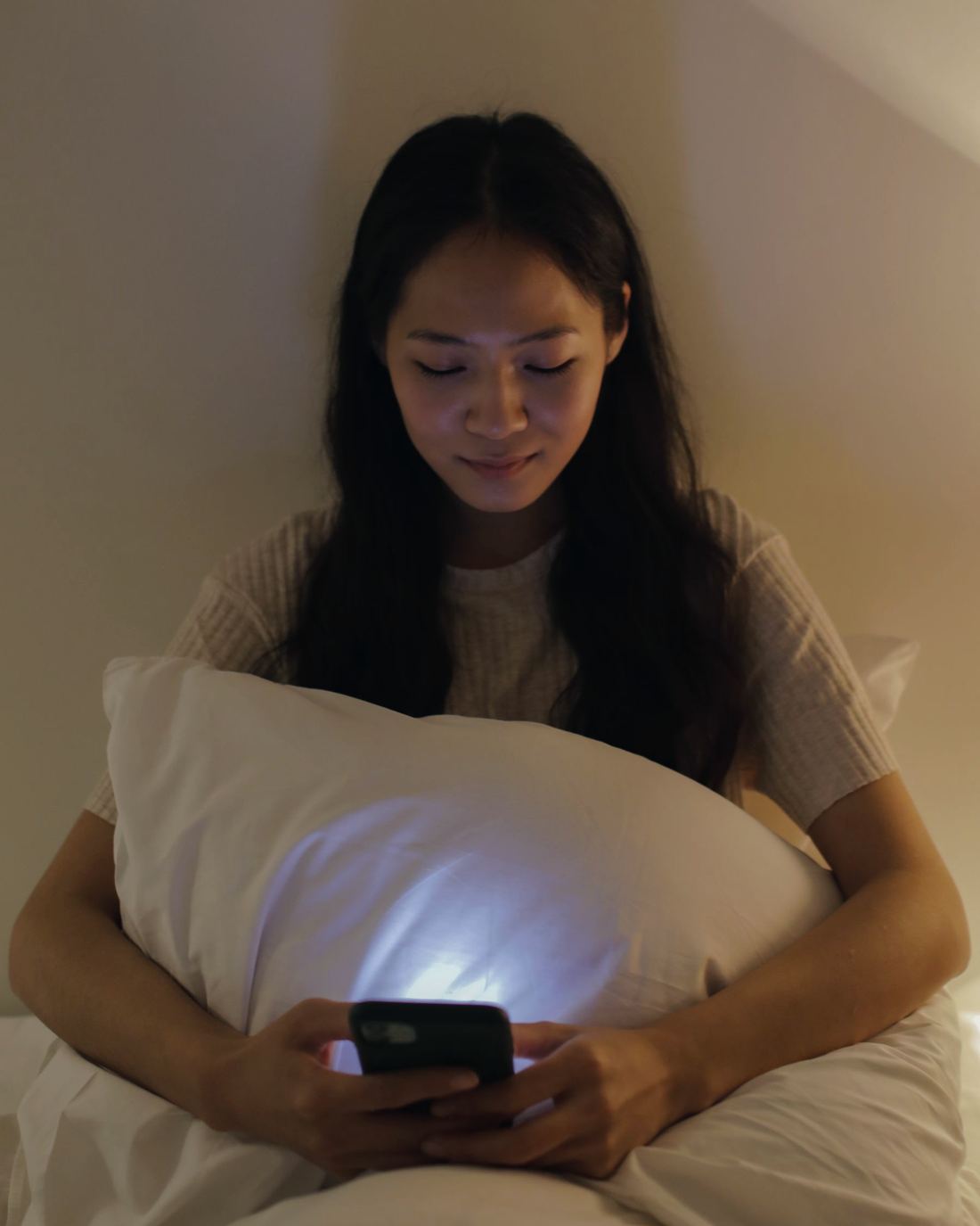 Una ragazza, la sera, legge il telefono stringendo un cuscino