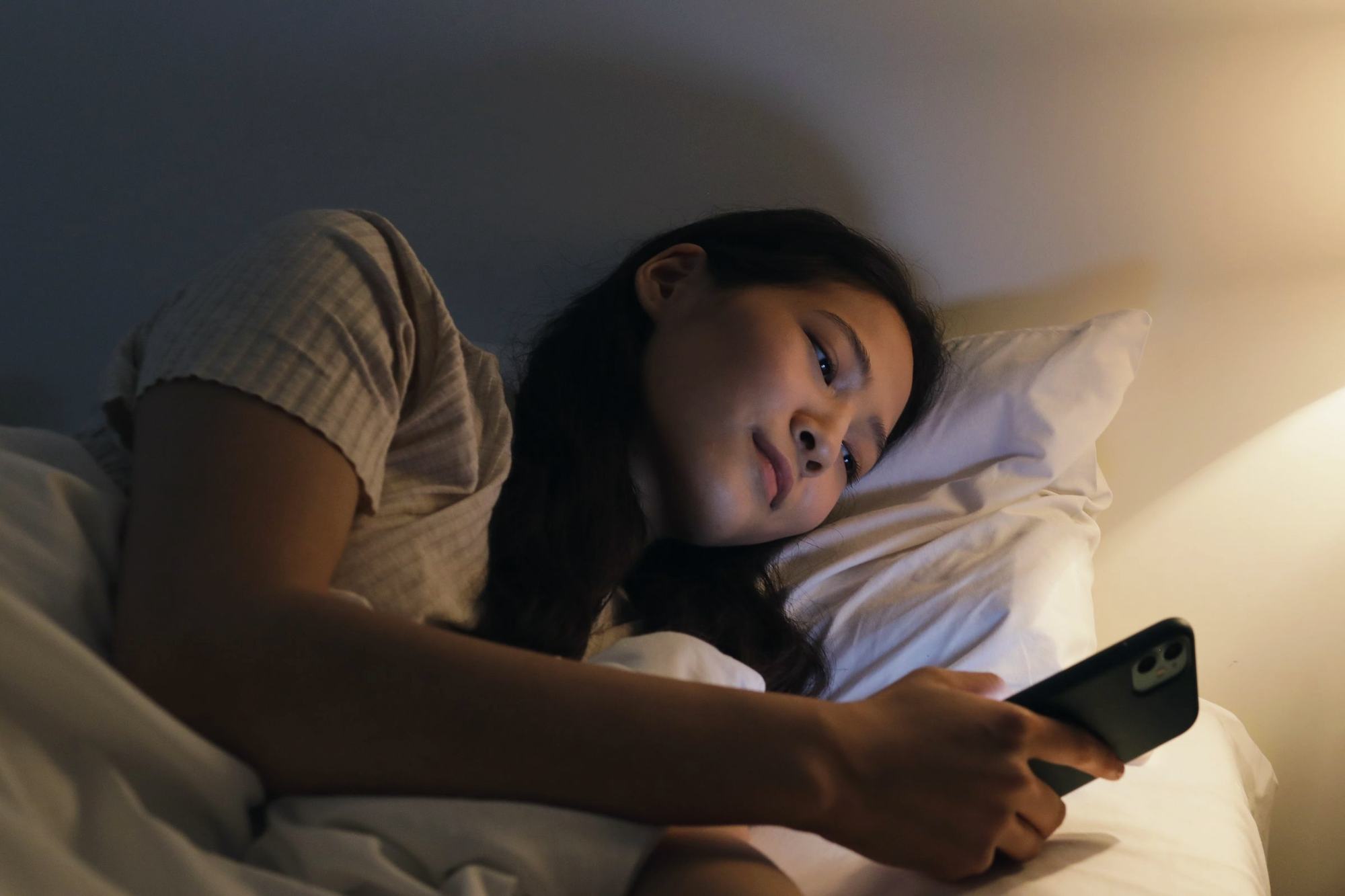 Una ragazza, la sera a letto, scrive dal telefono